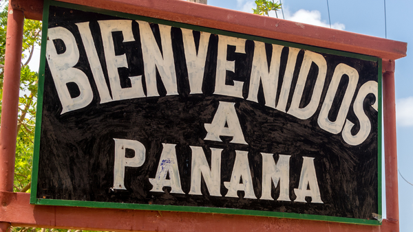 A sign with 'BIENVENIDOS A PANAMA' in bold white letters on a black background, welcoming to Panama, with a tropical setting in the background.