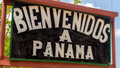 A sign with 'BIENVENIDOS A PANAMA' in bold white letters on a black background, welcoming to Panama, with a tropical setting in the background.